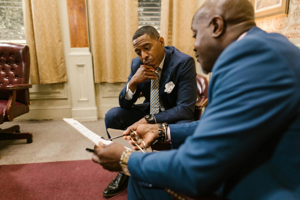 Two executives in business attire discuss documents in an office setting.